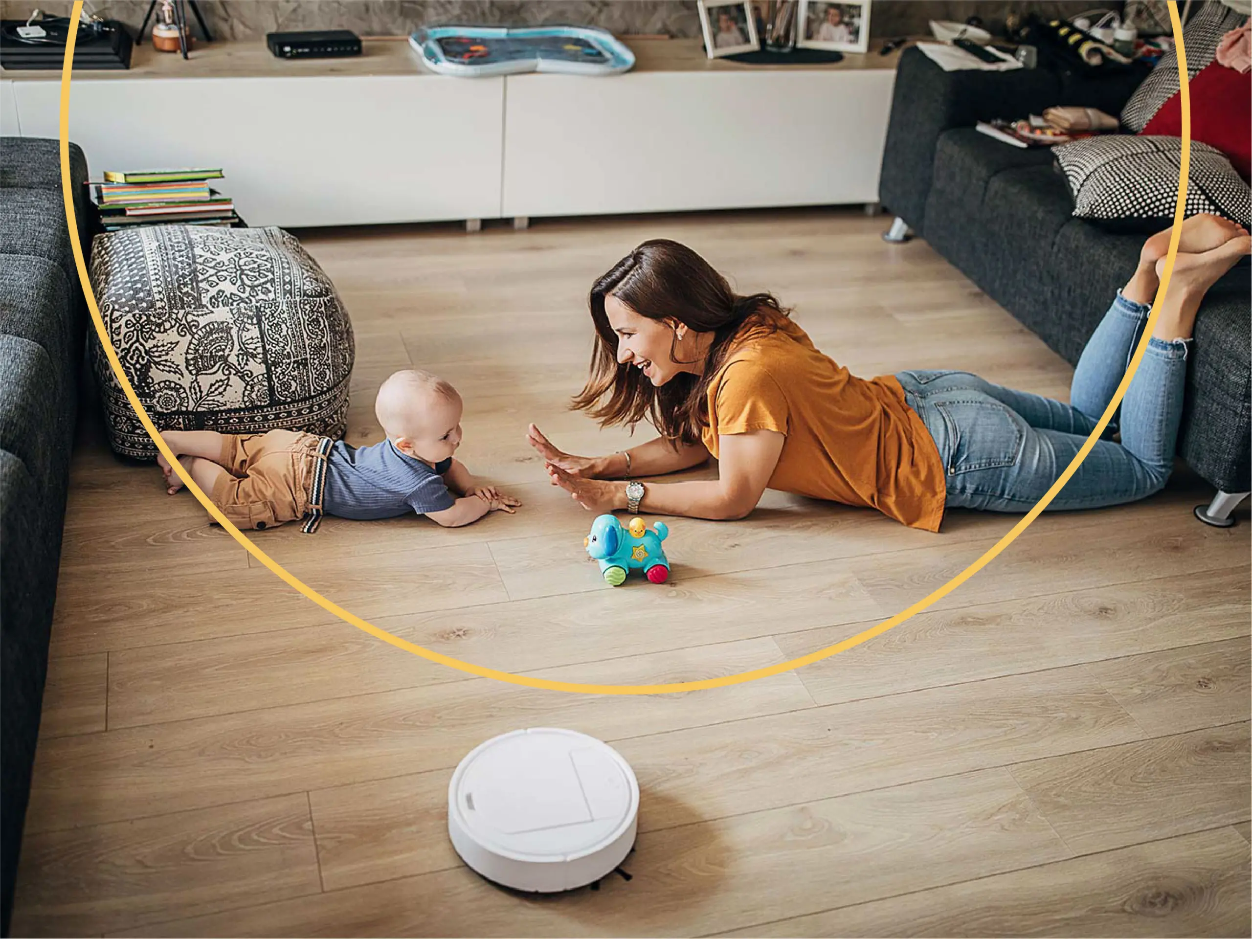 Mother and child play together on hardwood floors in the living room while a smart vacuum cleans the floors