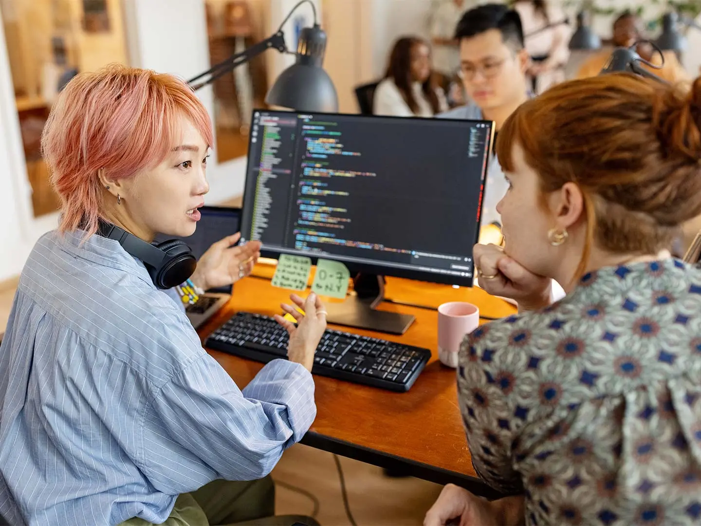 Female software developers discuss over the computer while sitting at a desk in the workplace. Creative businesswomen discuss the new coding program in the office.