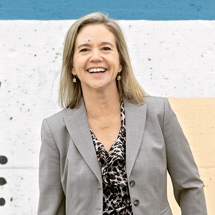 Professional headshot image of Meredith Bronk. The background behind Meredith is a mix of a black dotted pattern and blue and yellow stripes.