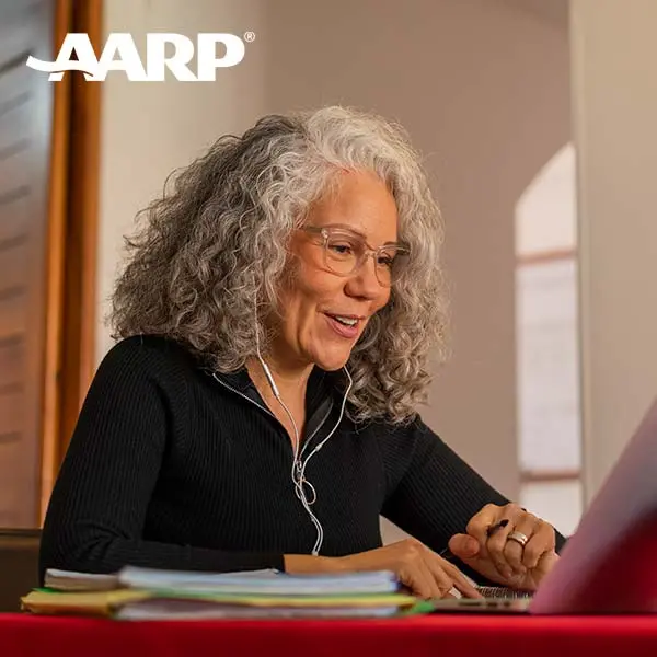 A woman interacting with the AARP website in their dining room with "AARP" logo is in the photo.