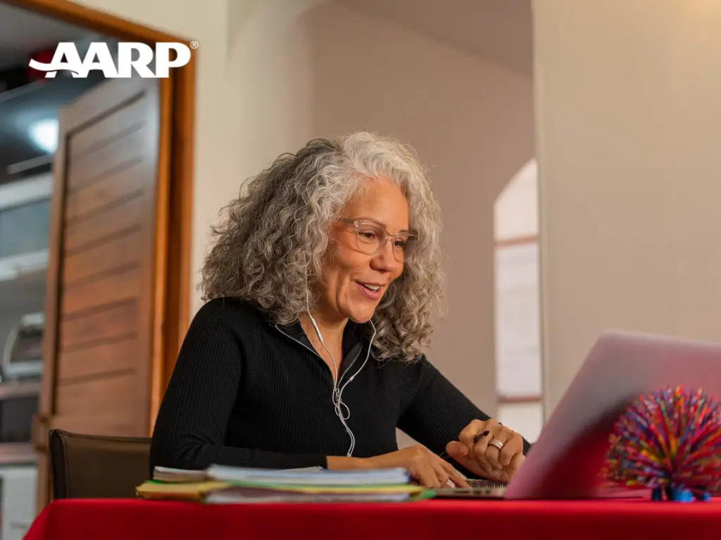 A woman interacting with the AARP website in their dining room with "AARP" logo is in the photo.
