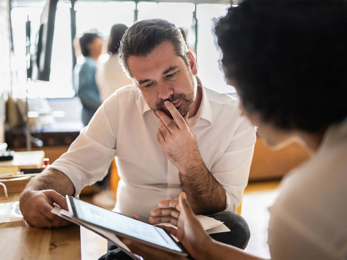 Mature man looking at a digital tablet that a colleague is showing at their workplace, a technology consulting firm.