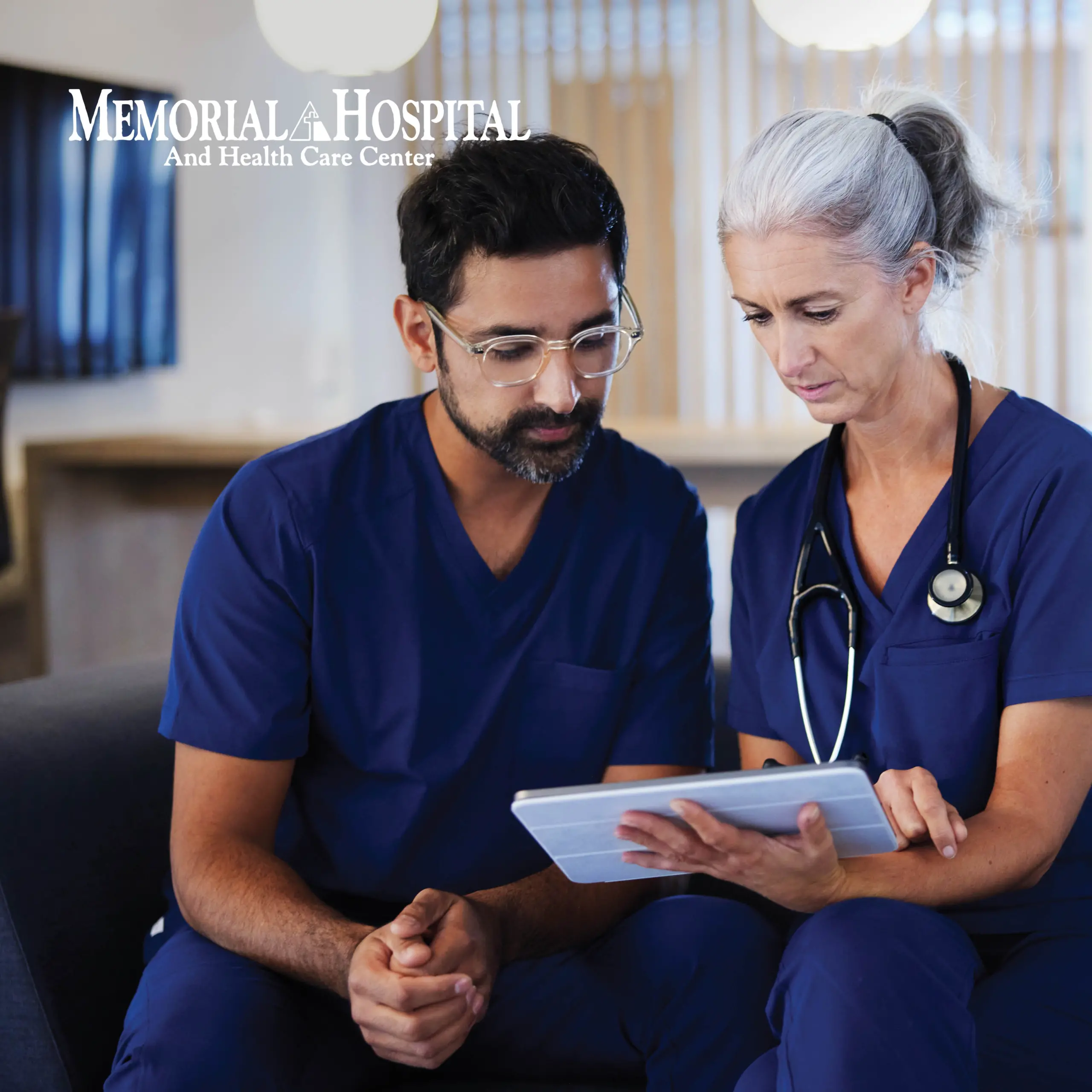 Two medical professionals with their stethoscope viewing information stored on the cloud via tablet. Text in the top left corner reads “Memorial Hospital And Health Care Center”.