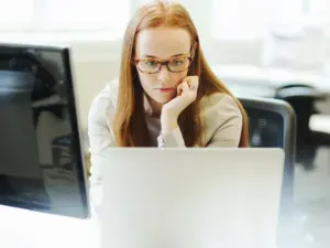Woman sitting at desk staring at two monitors with chin resting in her hand