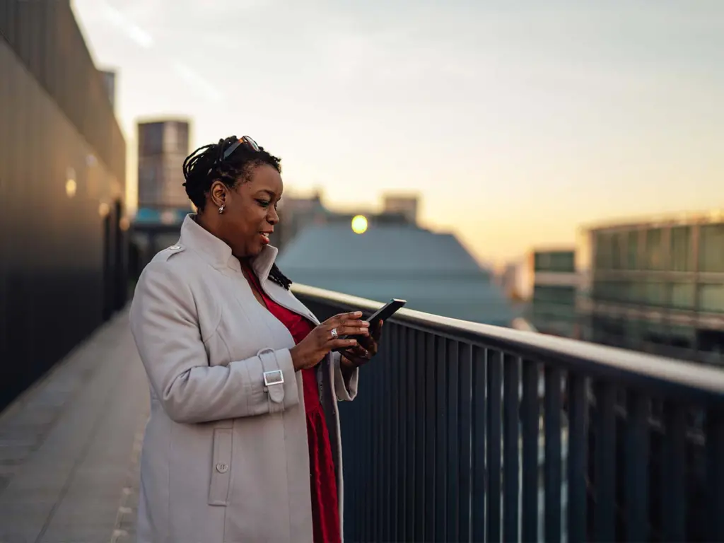 African adult female business professional standing on rooftop and talking on mobile phone.