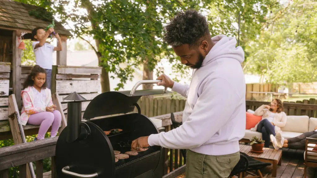 Family in backyard grilling with a connected product — smart smoker grill device.
