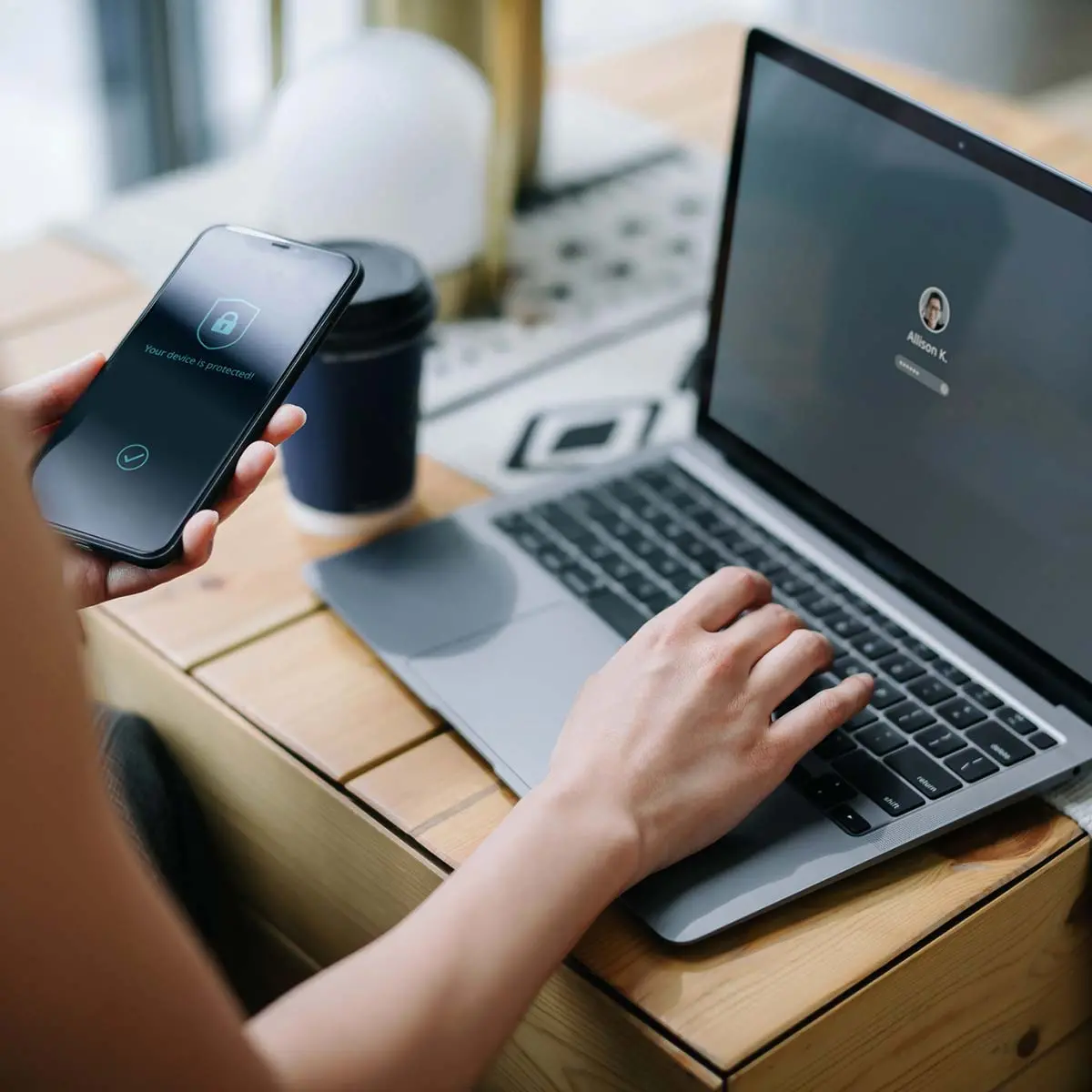 Young businesswoman working on desk, logging in to her laptop and holding smartphone on hand with a security key lock icon on the screen. Privacy protection, internet and mobile security concept