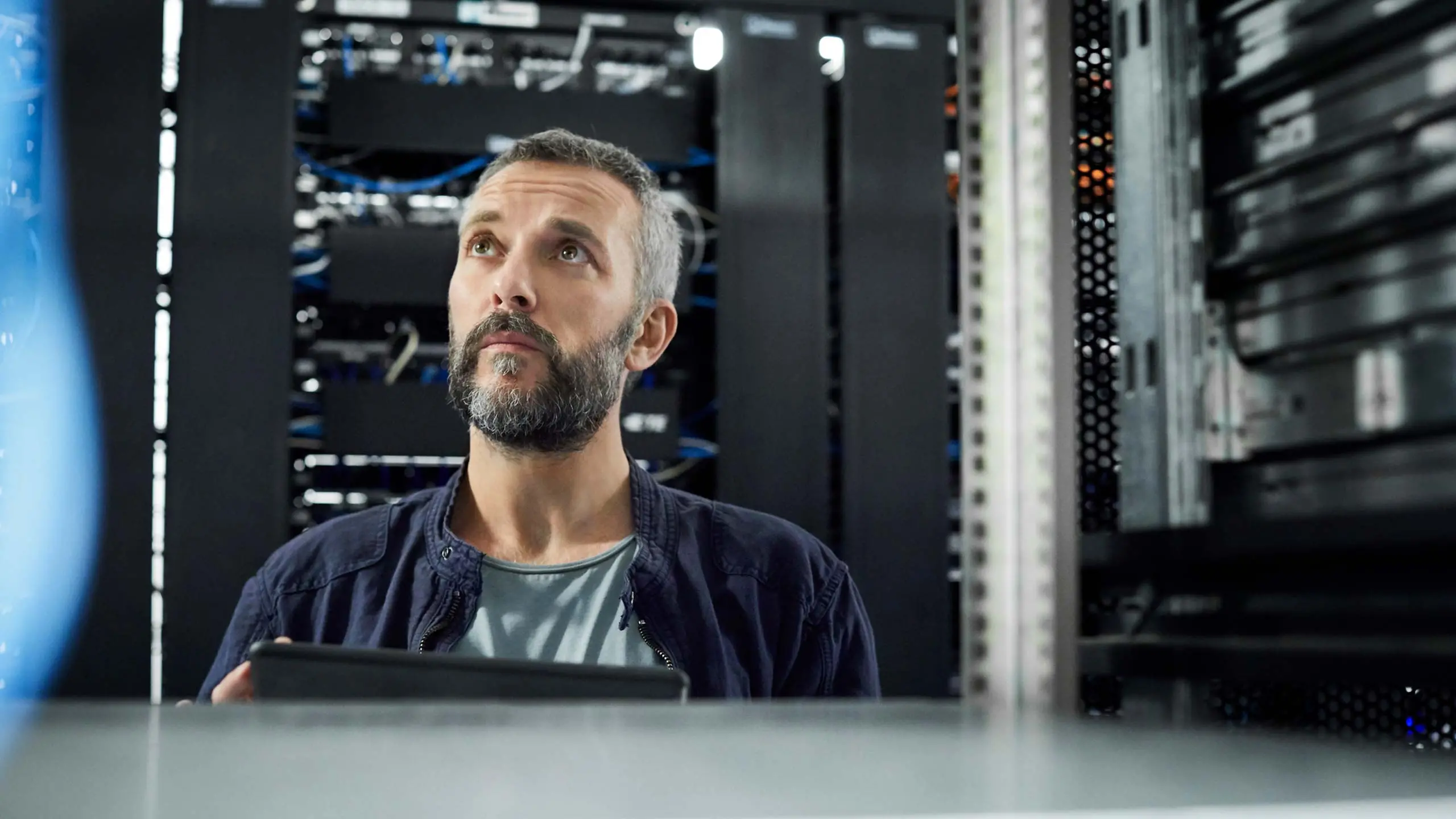 Male technician looking at cables. Engineer with laptop standing at workplace. He is in server room assessing cybersecurity.