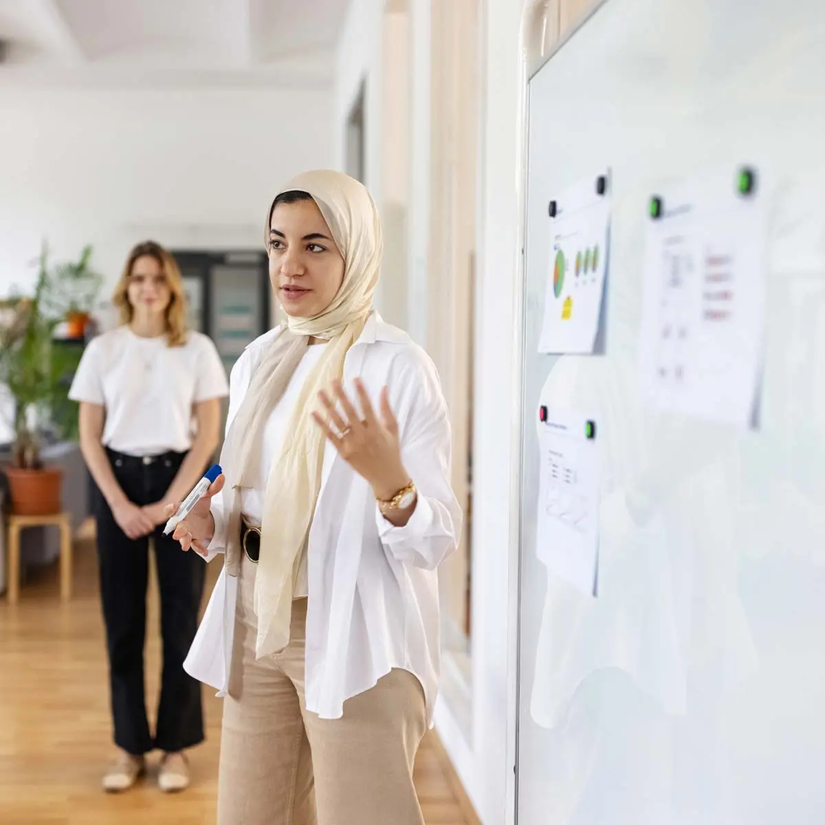 Woman in hijab explaining data analytics to colleagues in a presentation at startup office. Startup team having a planning meeting in hybrid office.