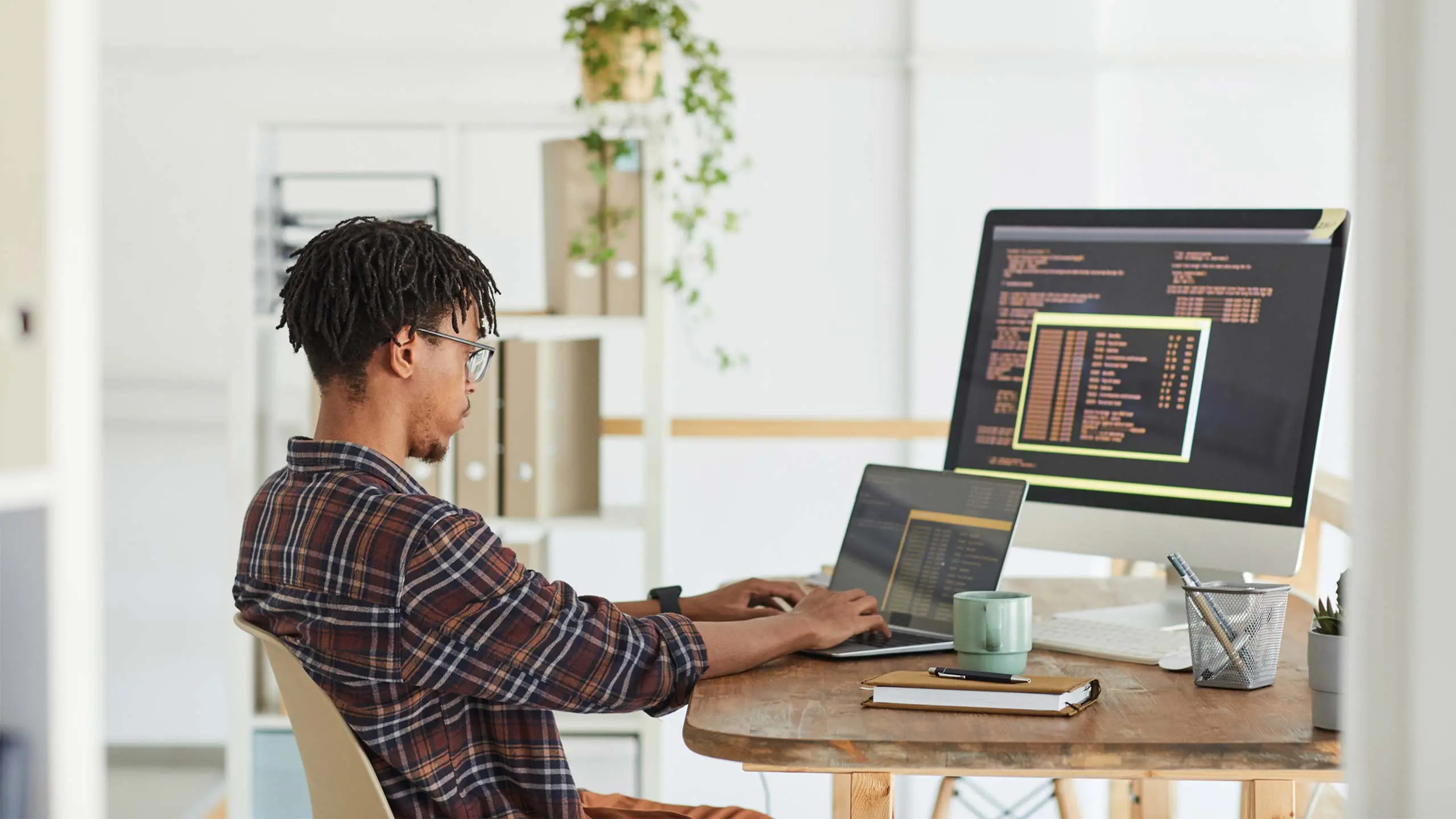 Side view at African-American IT developer typing on keyboard with black and orange programming code on computer screen and laptop, copy space