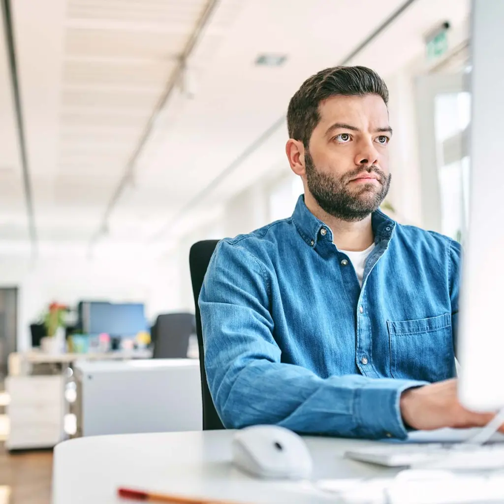 Confident mid adult businessman using computer. Male professional is working in creative office. He is wearing smart casual.