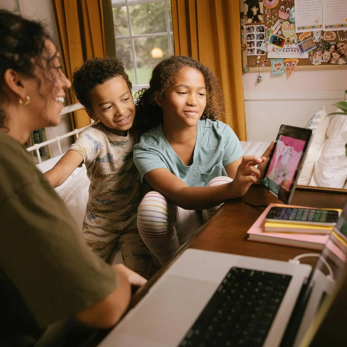 Siblings gathered at desk interacting with IoT tablet, laptop, phone.