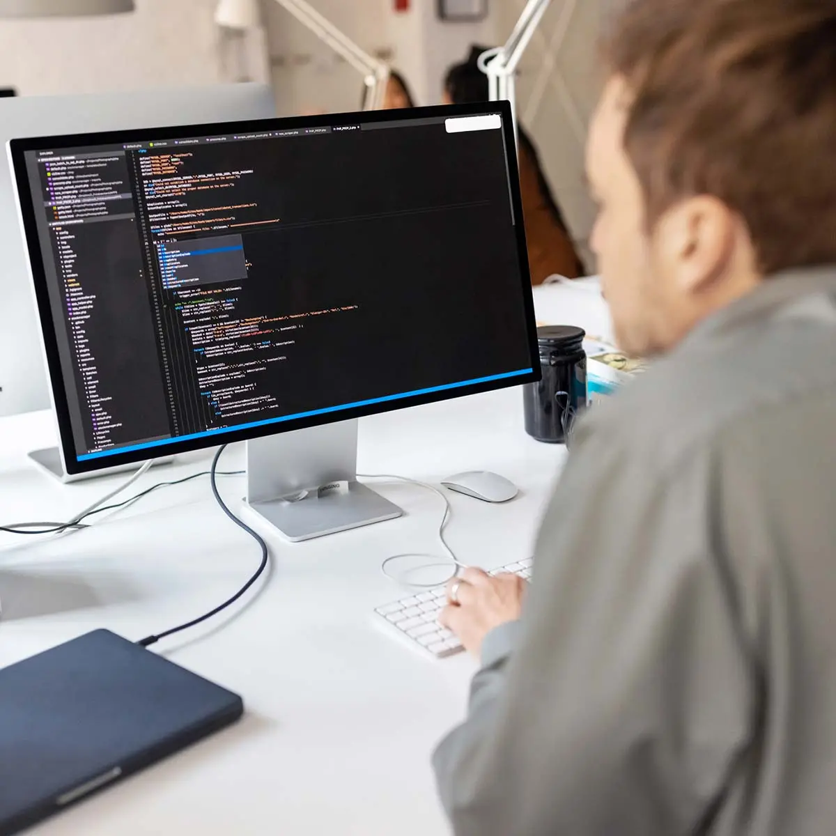 Rear view of a male software developer working on desktop computer writing code for mobile applications.