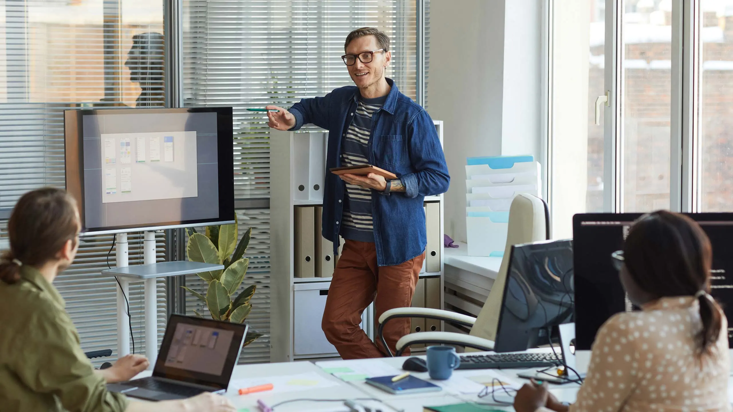 Portrait of contemporary businessman pointing at digital screen while giving presentation on strategic solutions at team meeting in IT development office, copy space