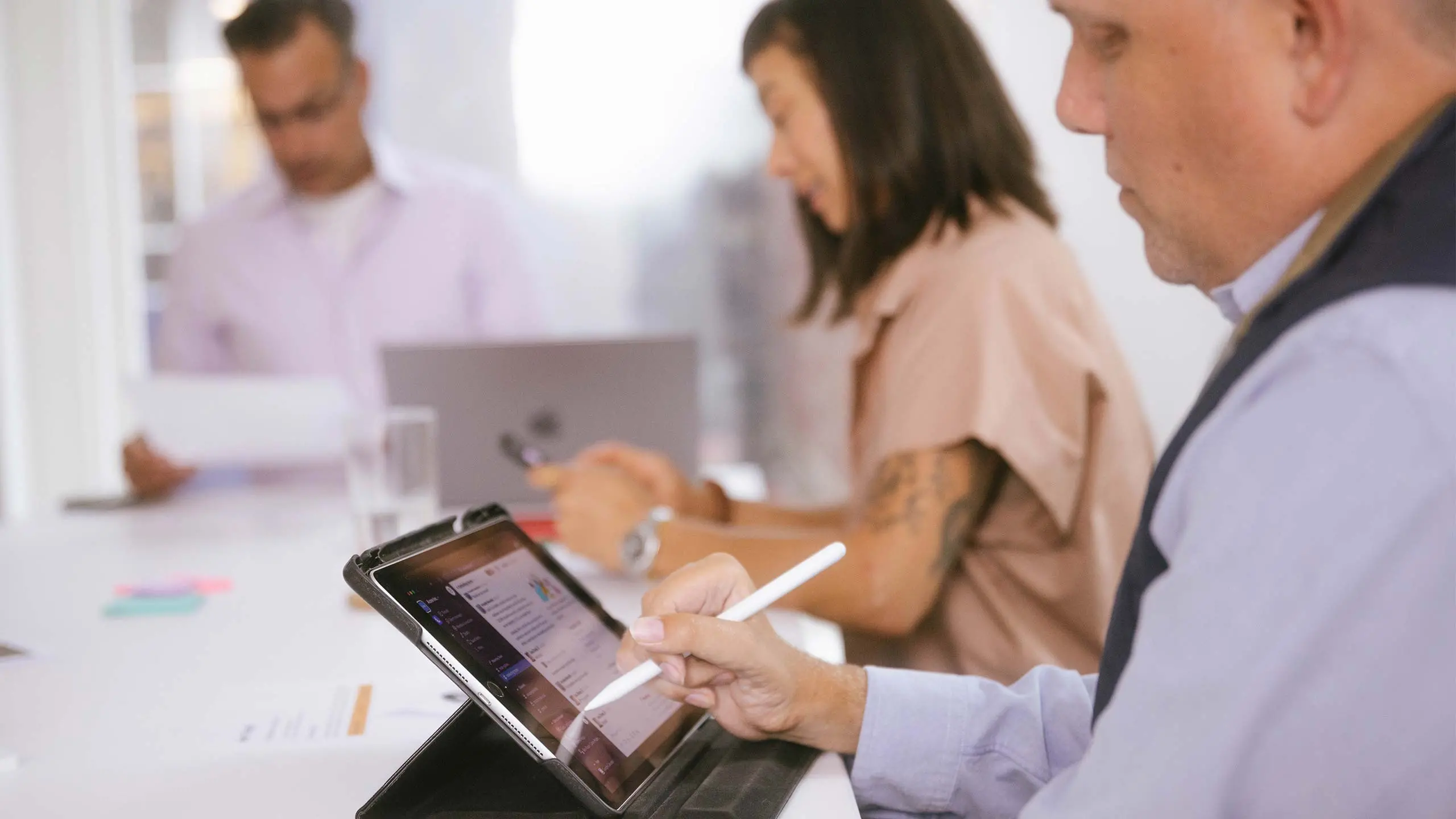 Coworkers collaborating around table. One person writing a digital product strategy on tablet.