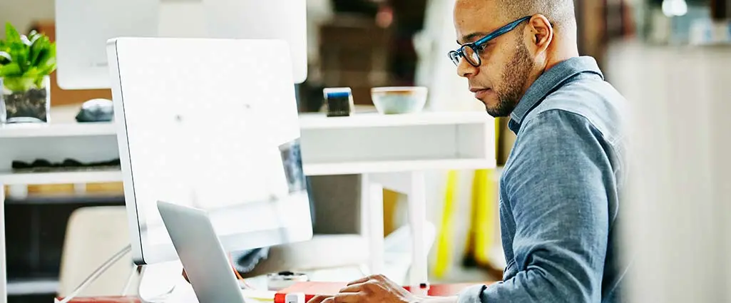 Businessman sitting at workstation in startup office working on project on laptop