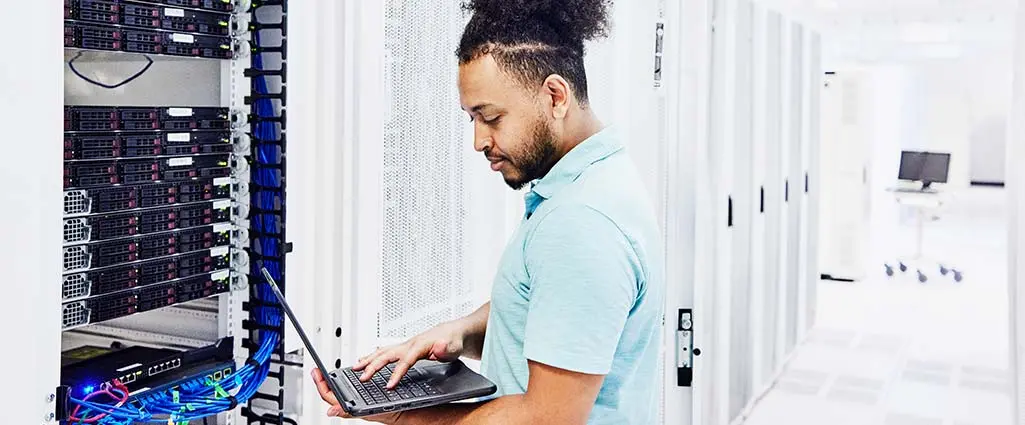 Medium shot of male IT professional looking at laptop while working on server in data center