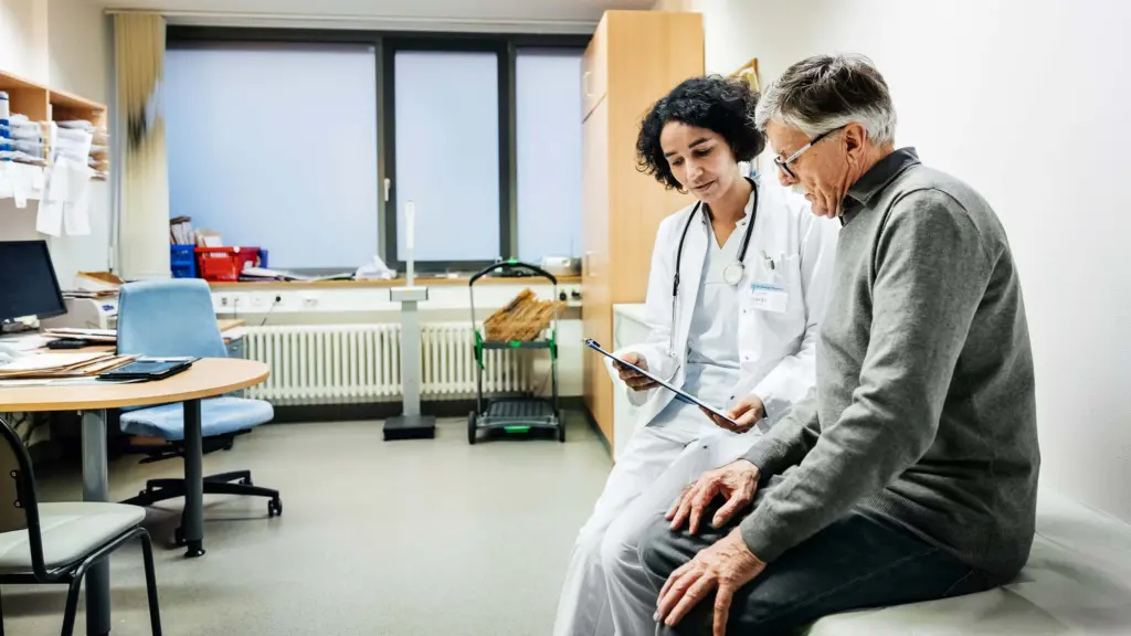 Doctor sitting alongside patient in office looking over tablet with health information