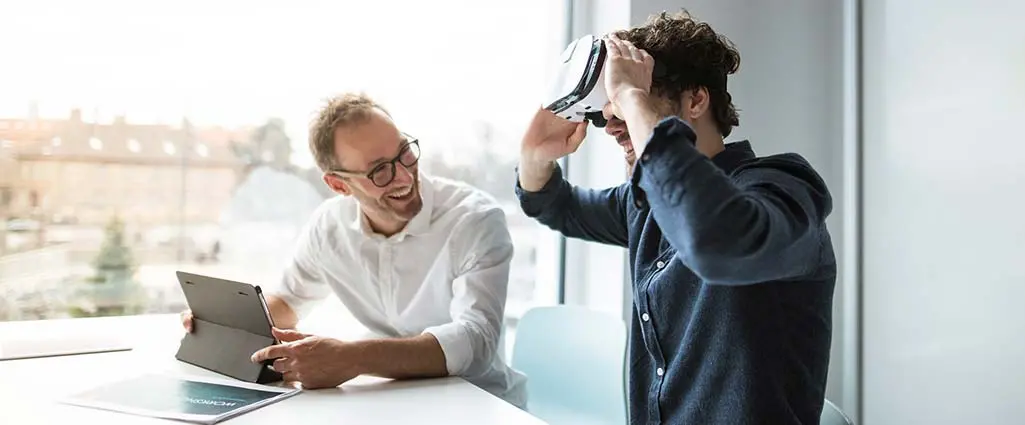 Smiling engineer looking at colleague examining virtual reality simulator in office