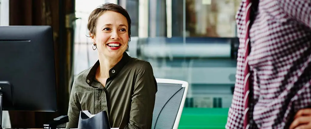 Smiling businesswoman sitting at workstation in discussion with coworker
