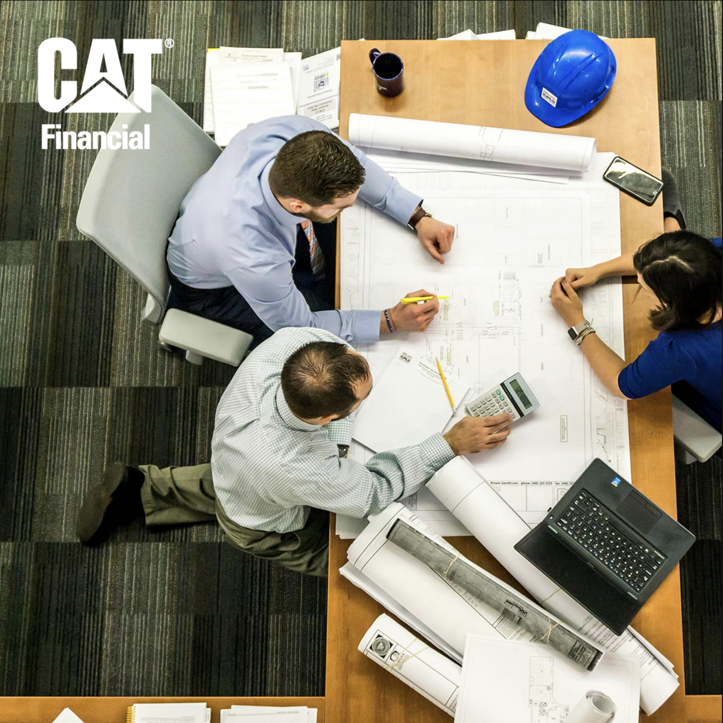 Three construction management employees looking over blue prints and calculator on conference table