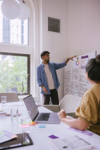Man presenting whiteboard ideas to woman in yellow blouse sitting at conference table